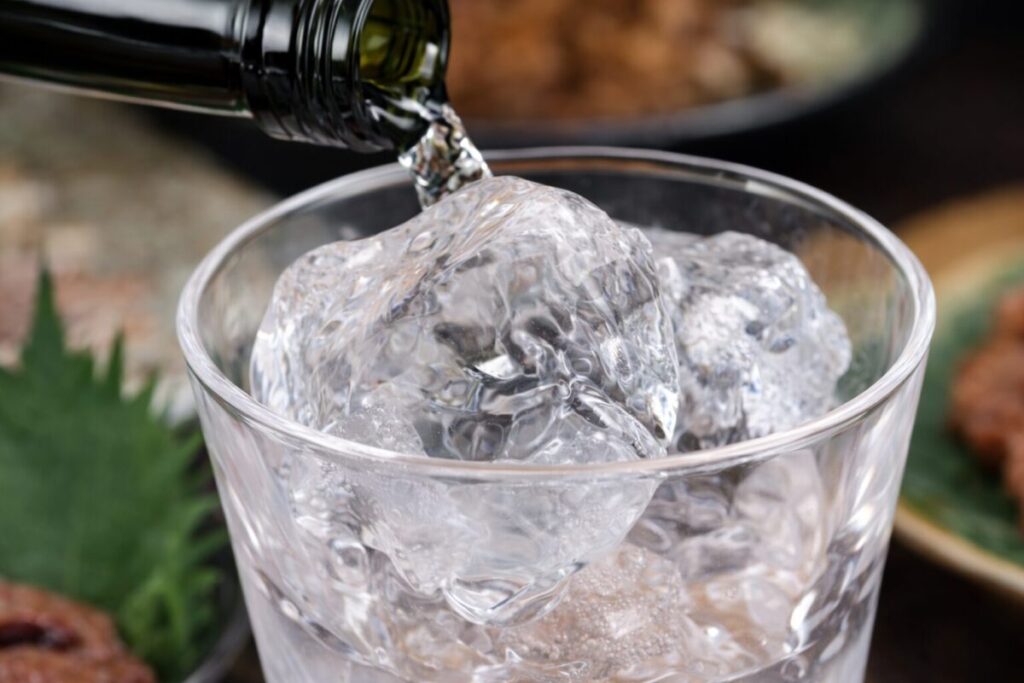 氷が入ったグラスにボトルから透明なお酒を注いでいる様子のクローズアップ画像