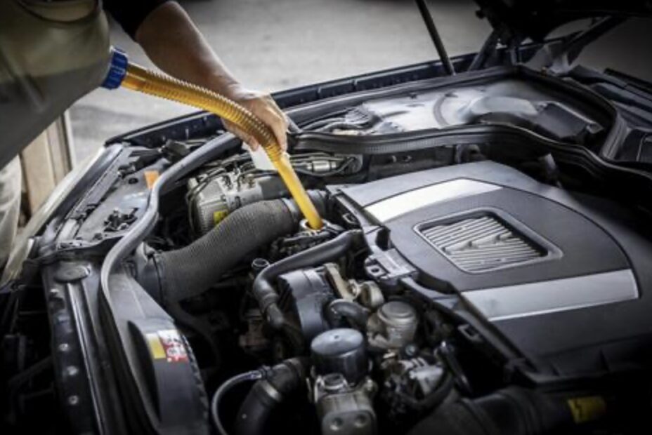 車のエンジンルームにオイルを注いでメンテナンスしている作業の様子